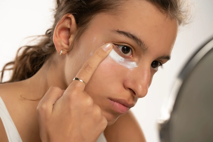 Retrato de jovem aplica produto cosmético sob os olhos em um fundo de estúdio branco
