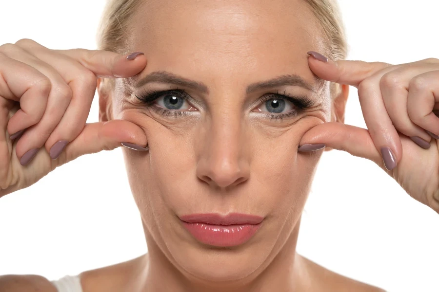 portrait of a middle aged woman pinching her wrinkles next to her eyes on a white studio background