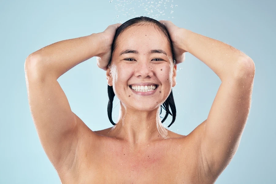 Dusche und glückliche Frau, die Haare im Studio wäscht, isoliert auf blauem Hintergrund