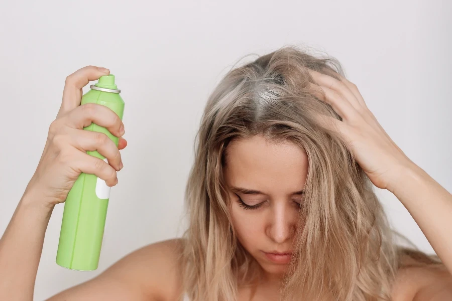 Jeune femme blonde aux cheveux gras sales pulvérisant du sel de mer