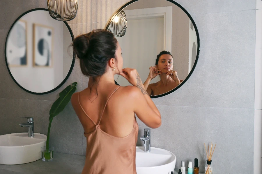 Mujer joven mirándose en el espejo y haciendo un masaje para esculpir la cara. Rutina de belleza matutina.