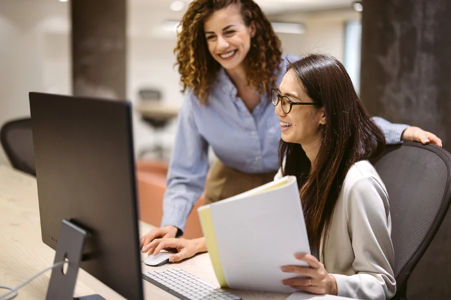 Dua wanita bekerja bersama di depan komputer di kantor