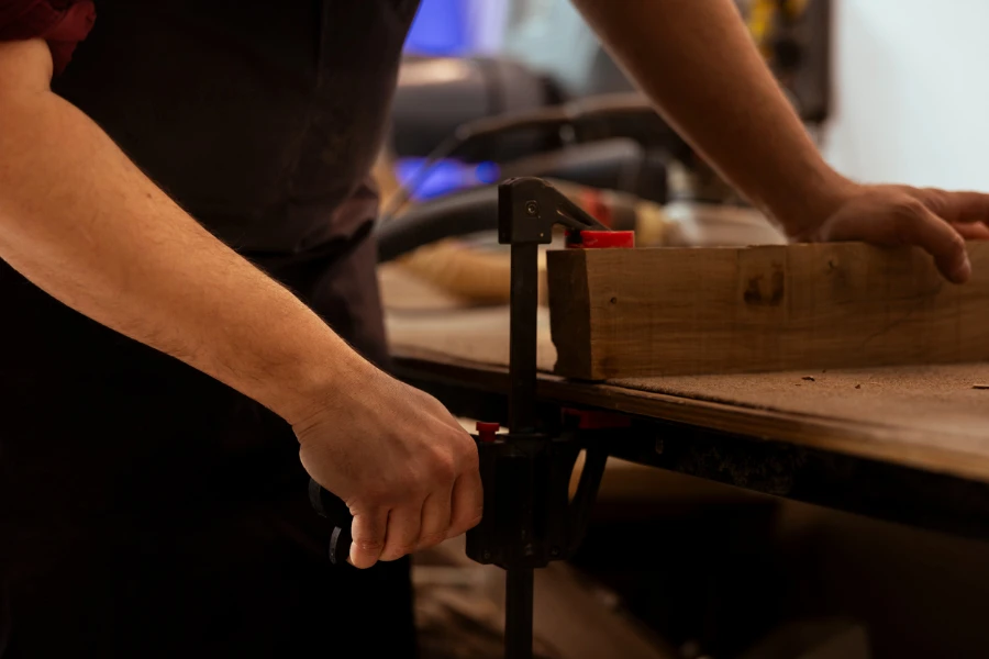 عامل نجارة يستخدم ملزمة مقاعد البدلاء لإمساك كتلة الخشب