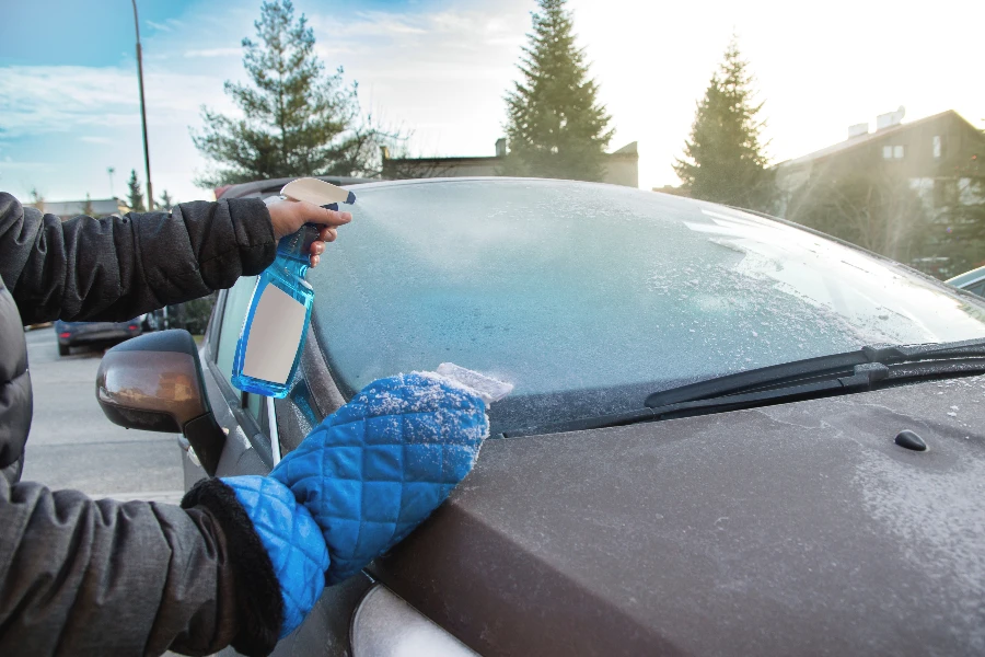 A man's hand scraping front car window on an icy day