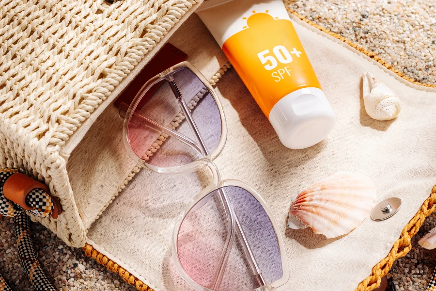Protetor solar e óculos em um saco de palha de vime em uma praia arenosa