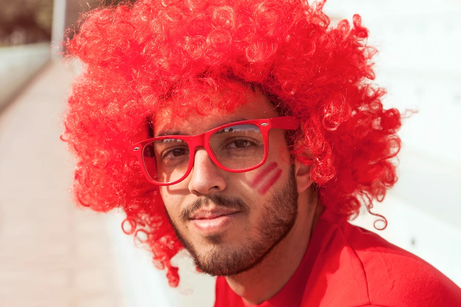 portrait of fan with red wig and glasses sitting on the stands of a stadium