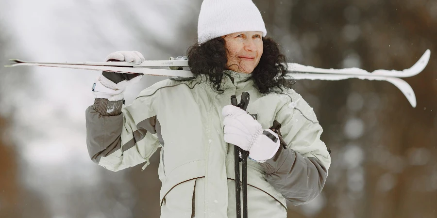 Женщина в куртке держит лыжи