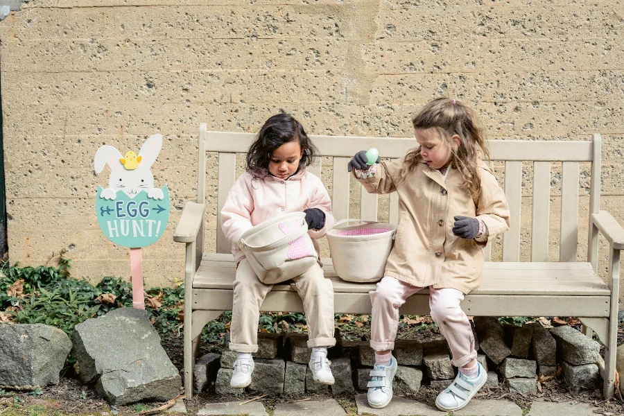 Mädchen in warmer Kleidung spielen mit Ostereiern und sitzen auf einer Bank im Hinterhof