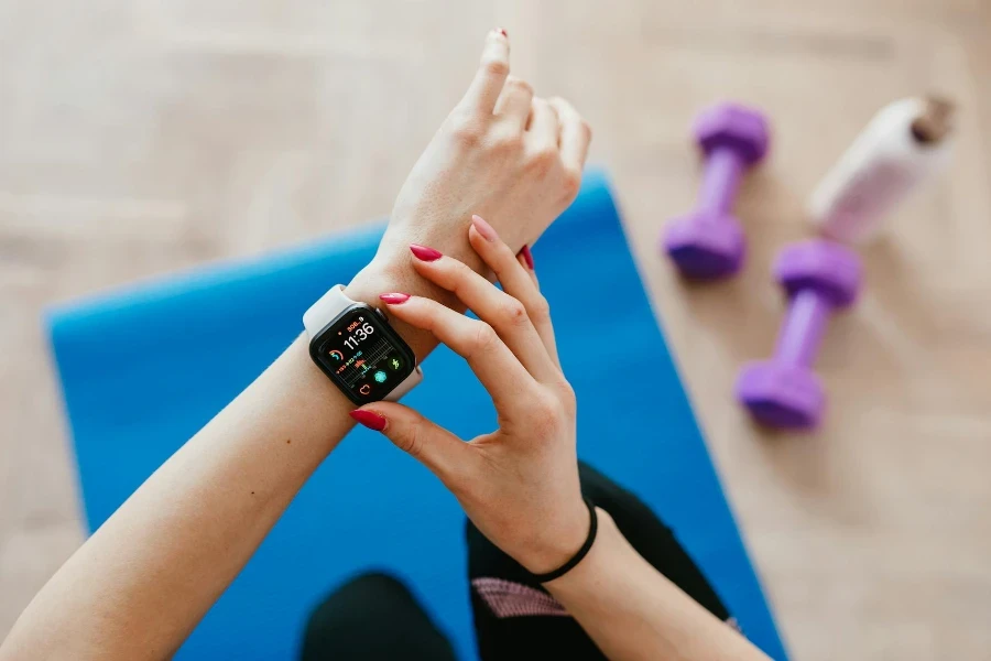 Sportive anonyme vérifiant la montre intelligente et assise sur un tapis