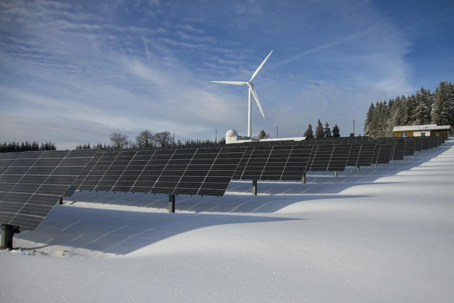 Painéis solares na neve com moinho de vento sob céu claro