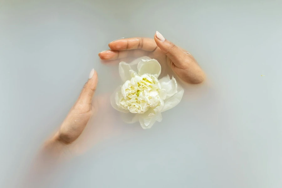 Unerkennbare Frau mit manikürten Händen, die während Spa-Behandlungen eine weiße Blume in Seifenwasser hält