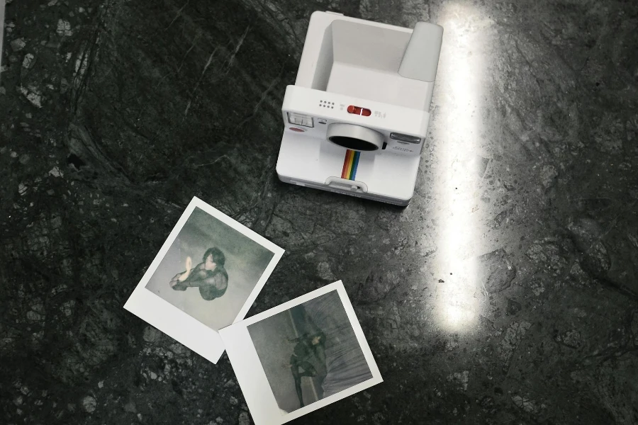 Modern instant photo camera and photos placed on marble surface