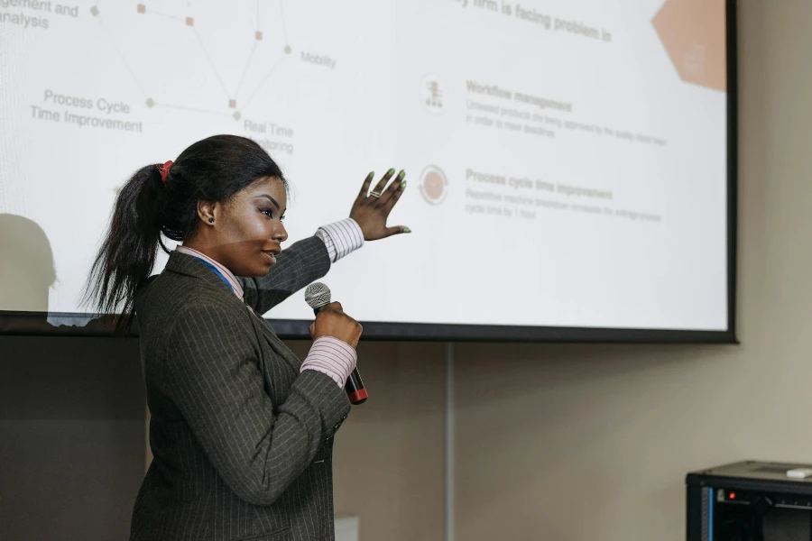 Uma mulher segurando um microfone enquanto mostra a tela do projetor