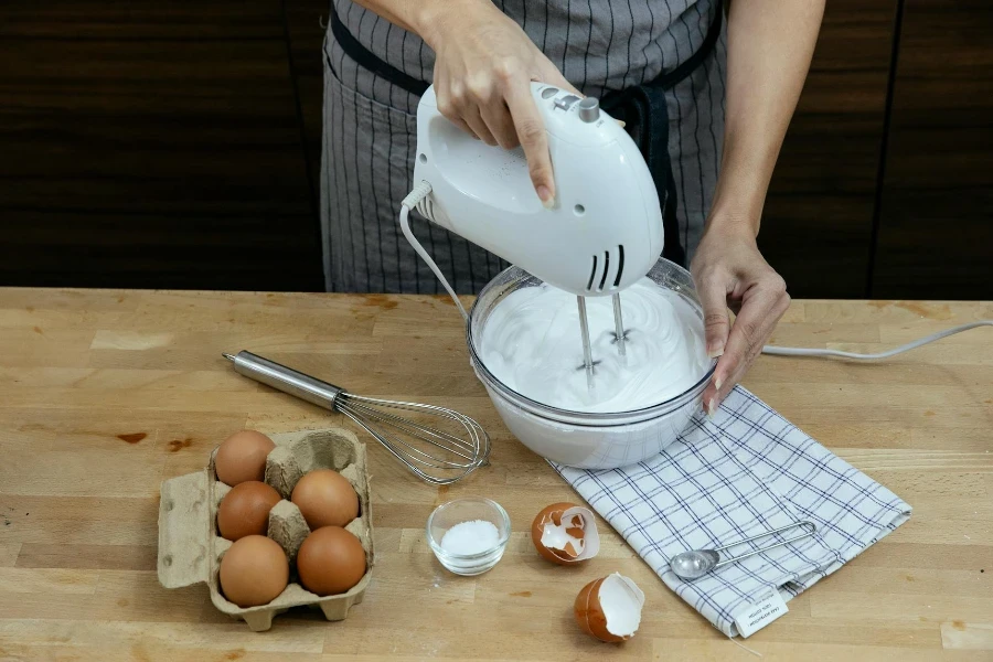 chef femenina en delantal batiendo huevos y preparando crema batida esponjosa