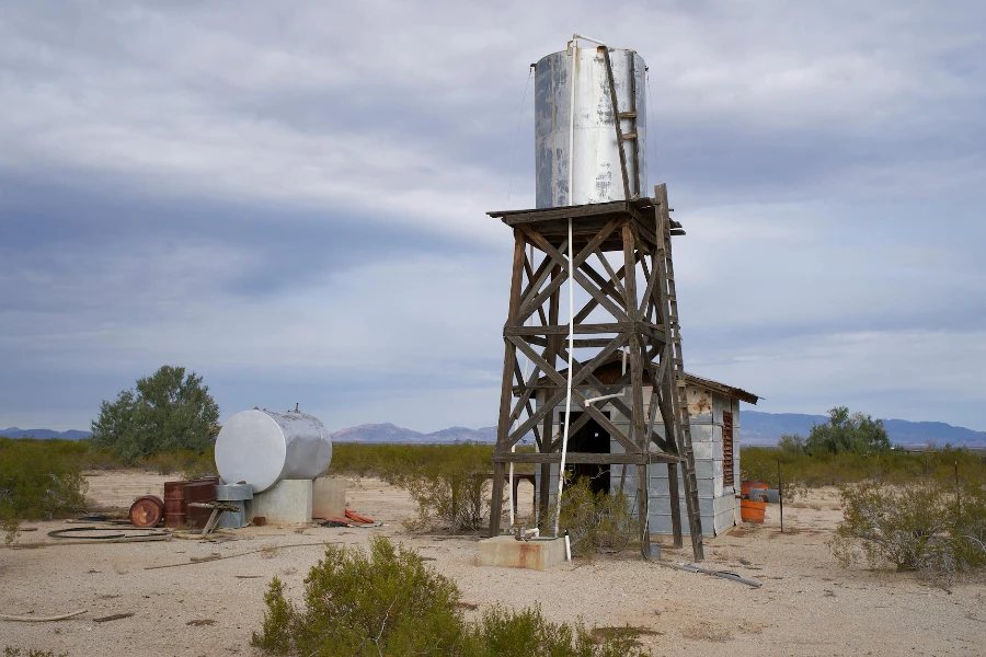 Ein verlassener und rostiger Wassertank und ein Gebäude in einer Wüste