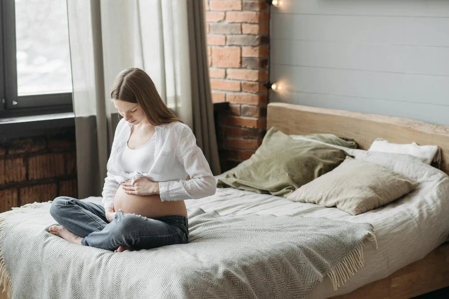 Donna incinta seduta sul letto che tiene la pancia