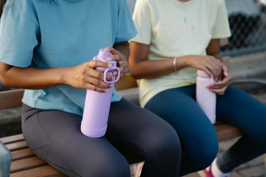 People Sitting on a Bench while Holding Tumblers