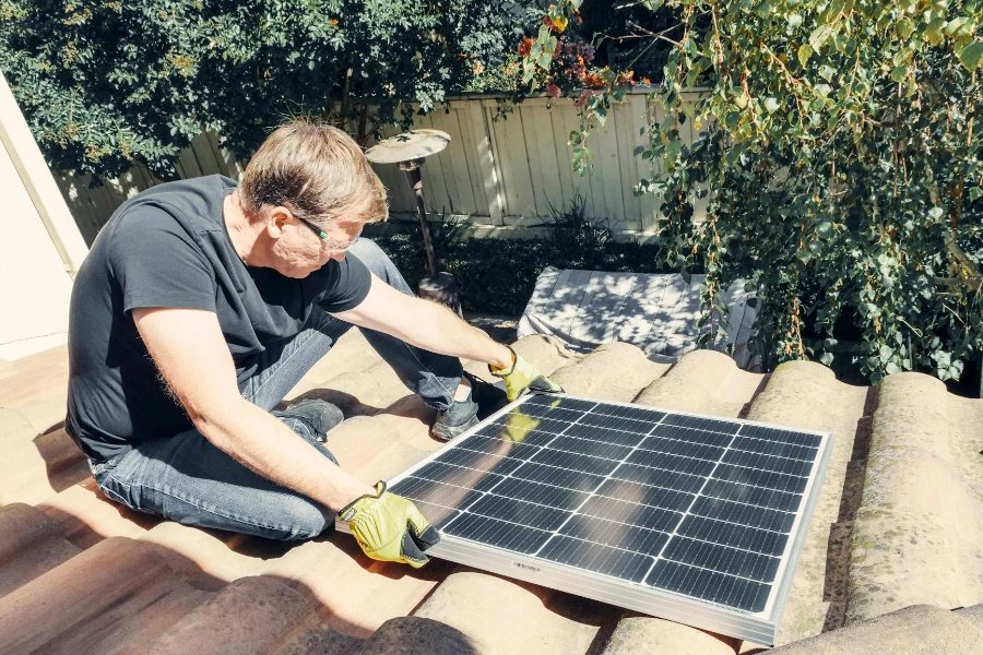 Un uomo in camicia nera seduto sul tetto mentre tiene in mano un pannello solare