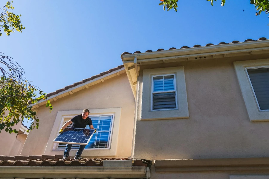 Um homem parado no telhado enquanto segura um painel solar