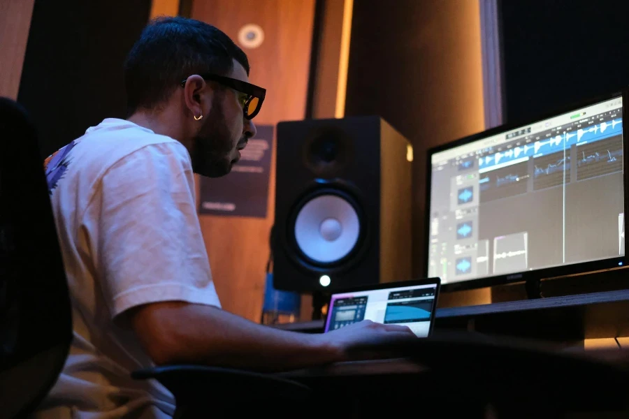 Man Working in White Shirt Sitting in Front of a Monitor and Speaker