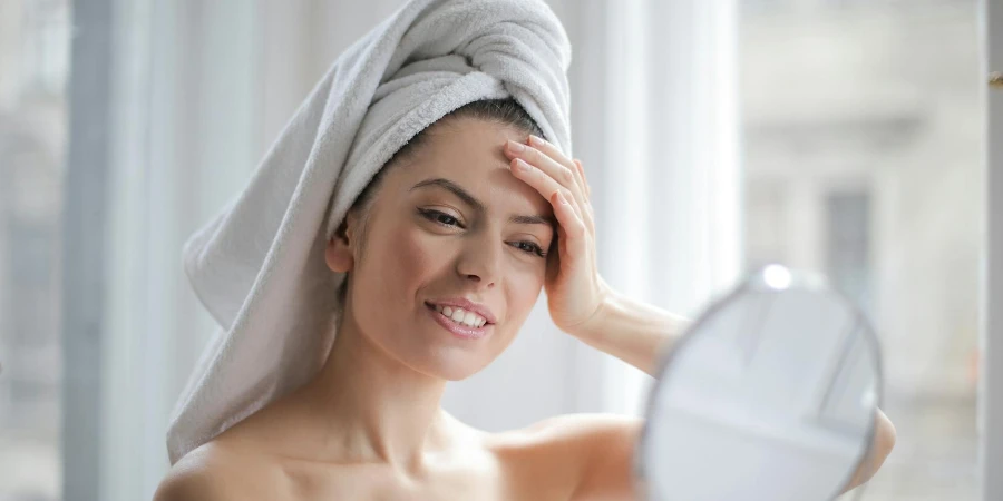タオルを頭に乗せて鏡を見ている笑顔の女性の選択フォーカスポートレート写真
