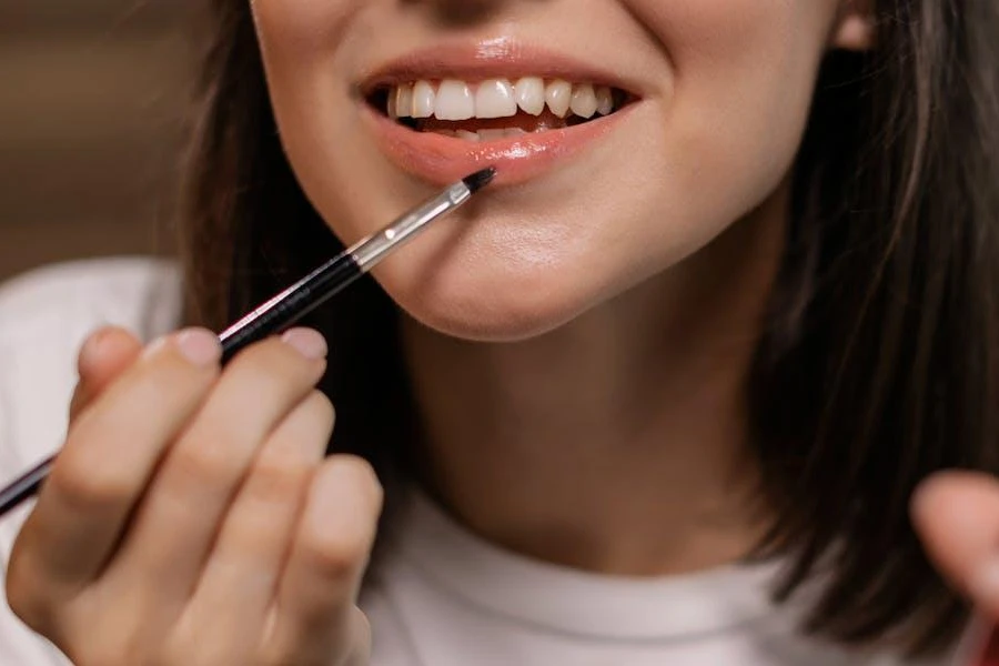 Smiling woman applying lip gloss with a brush