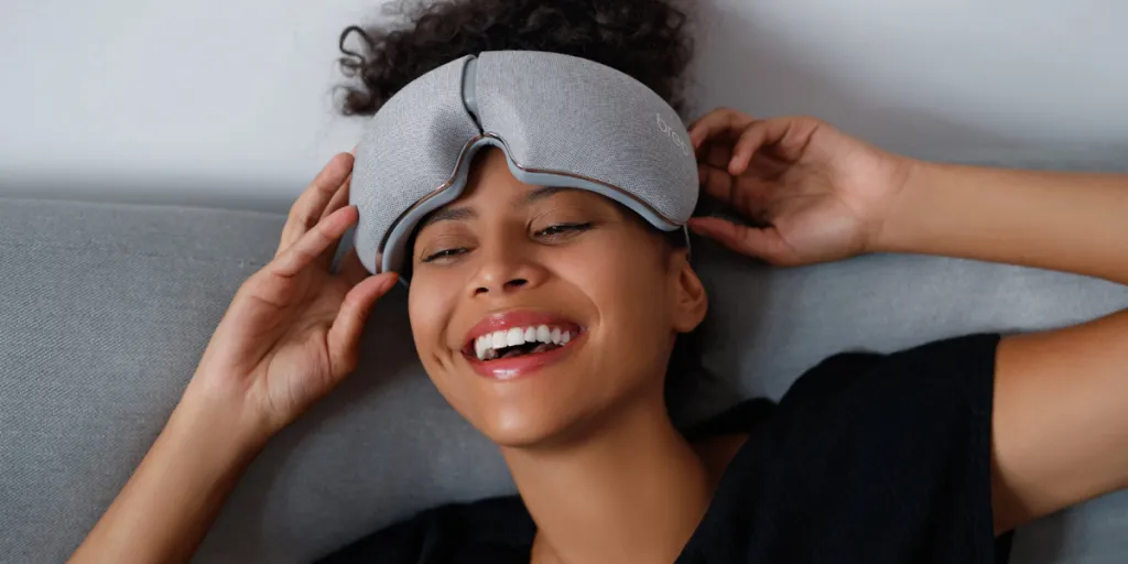 Lächelnde Frau mit einem Augenmassagegerät auf dem Kopf