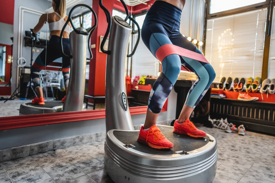 Güç plakası makinesi üzerinde eğitim alan bir kadın, bacaklar ve alçak bölüm egzersizi için güç plakası kullanıyor