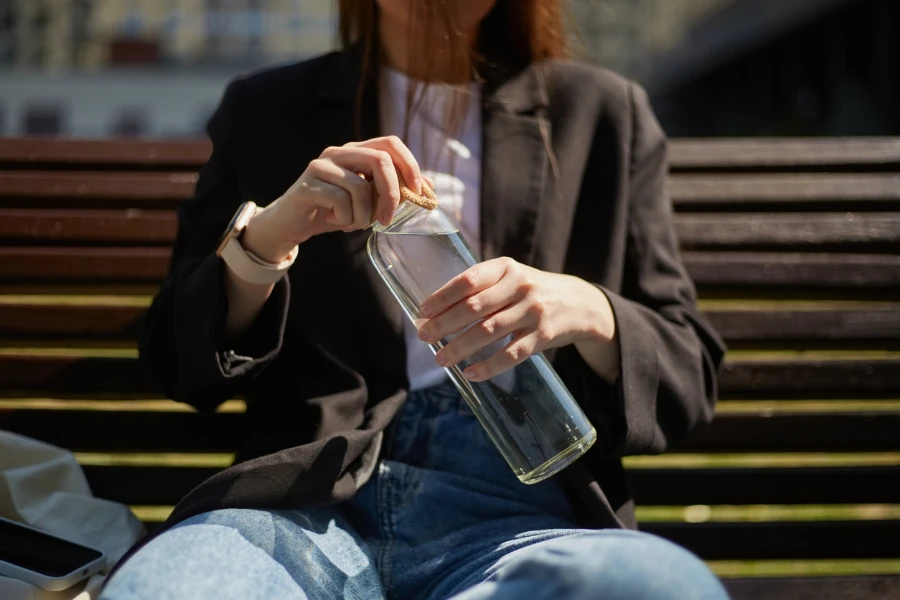 Young Ukrainian female person in early 20s using modern gadgets for freelance work and reusable glass bottle for hydration