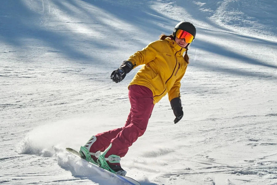 Eine Person in gelber Jacke mit Schutzbrille fährt auf einem schneebedeckten Boden Ski