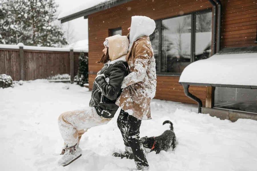 Eine Seitenansicht eines Paares in Winterkleidung, das mit ihnen auf einem schneebedeckten Boden spielt