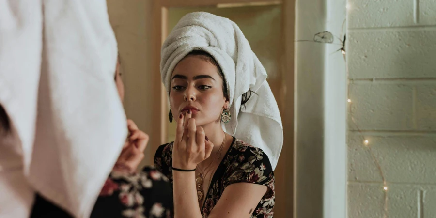 Una mujer aplicándose maquillaje frente a un espejo.