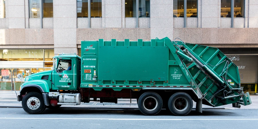 A large green trash truck in the streets of Manhattan