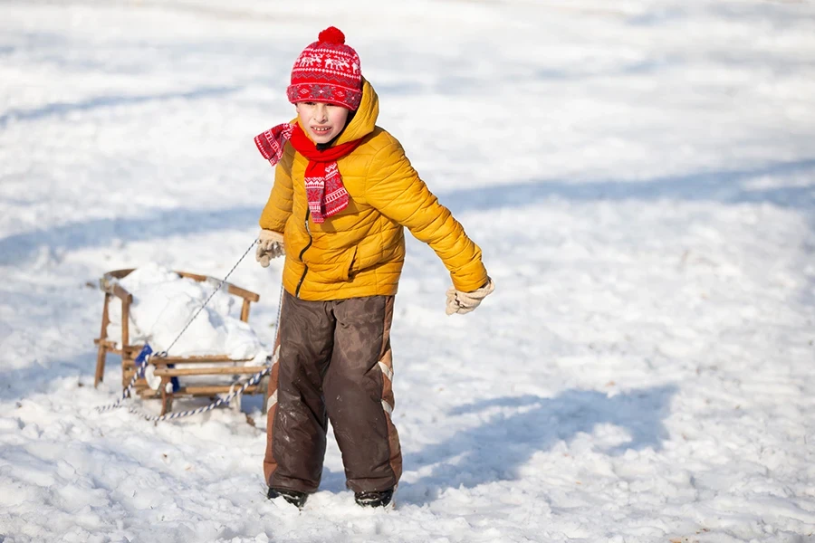 Un niño pequeño y divertido viaja en un trineo de madera en el pueblo en un día de invierno.