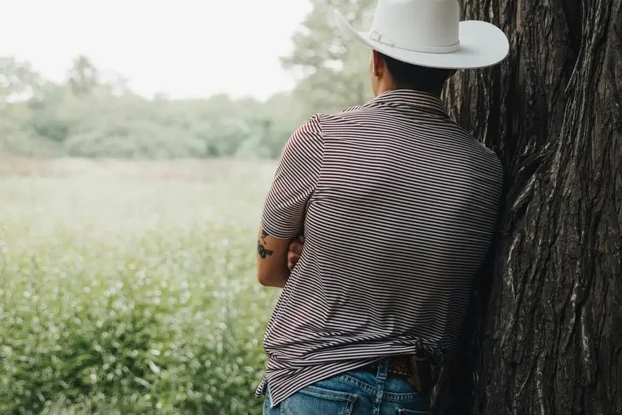 Ein Mann mit Cowboyhut lehnt an einem Baum von Eli Villarreal