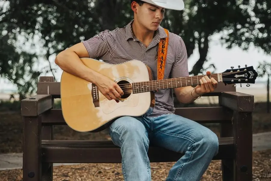 Un uomo con cappello da cowboy seduto su una panchina suona la chitarra di Eli Villarreal