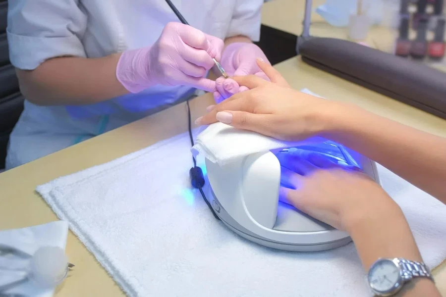 A manicurist is doing a manicure for a woman, using a UV manicure lamp on the table