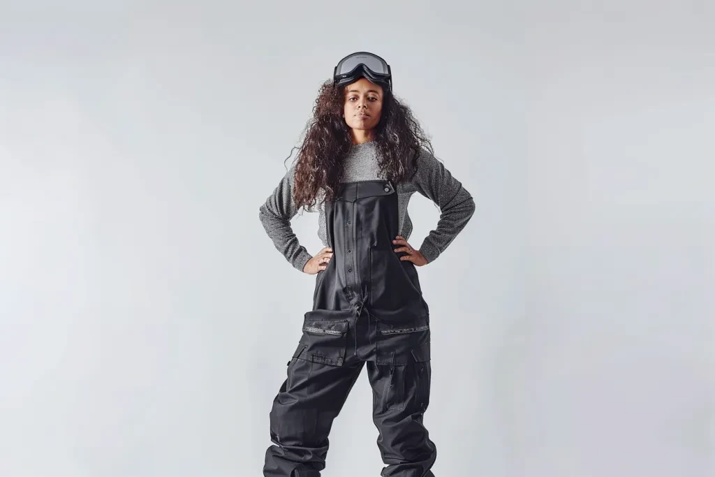 A woman wearing black snow overalls in a full body shot against