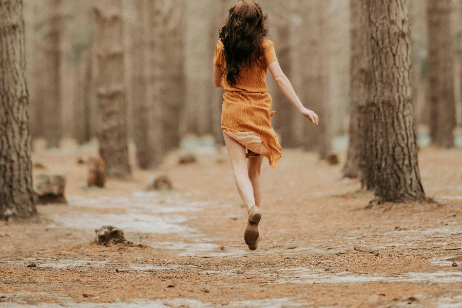 Erwachsene Frau läuft im Kleid zwischen Bäumen
