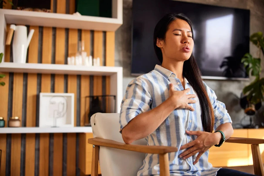 Eine asiatische Frau macht eine morgendliche Atemtechnik mit Handauflegen auf Brust und Bauch