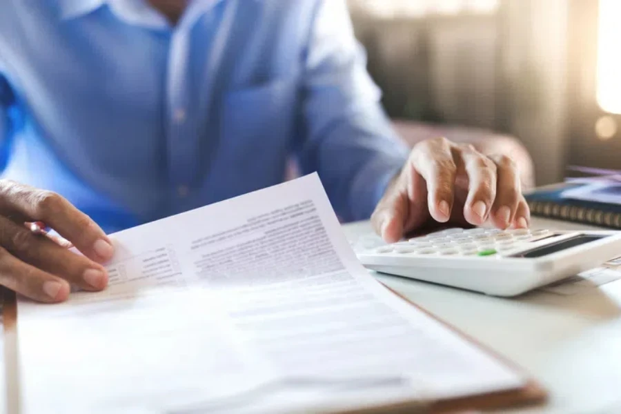 Empresário asiático na mesa do escritório usando calculadora para calcular benefícios ou despesas de seguro de vida a partir de extratos e relatórios financeiros