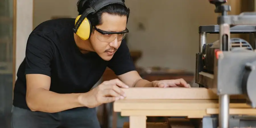 Attentive Asian joiner leveling timber on planer in workshop by Ono Kosuki