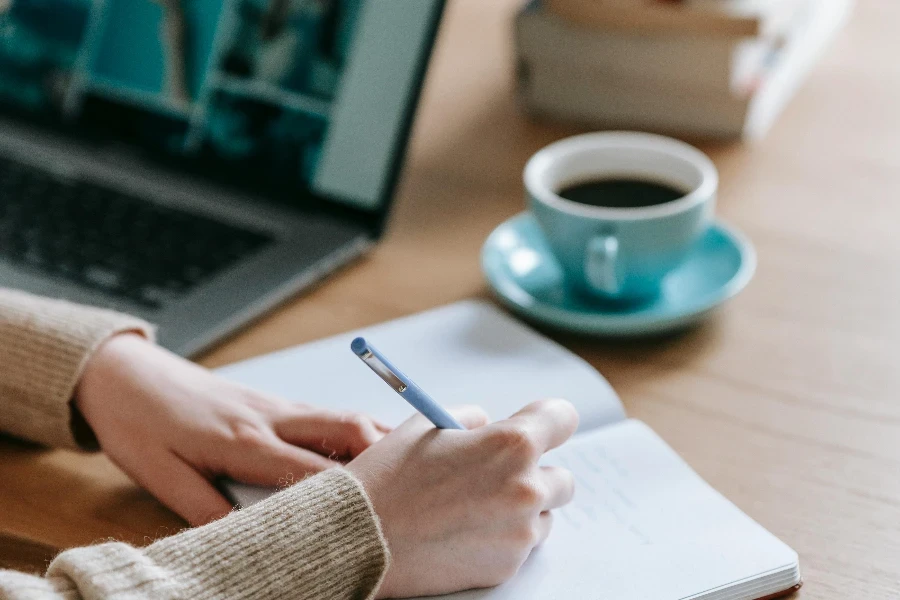 Businesswoman writing thoughts in empty notebook near laptop and coffee