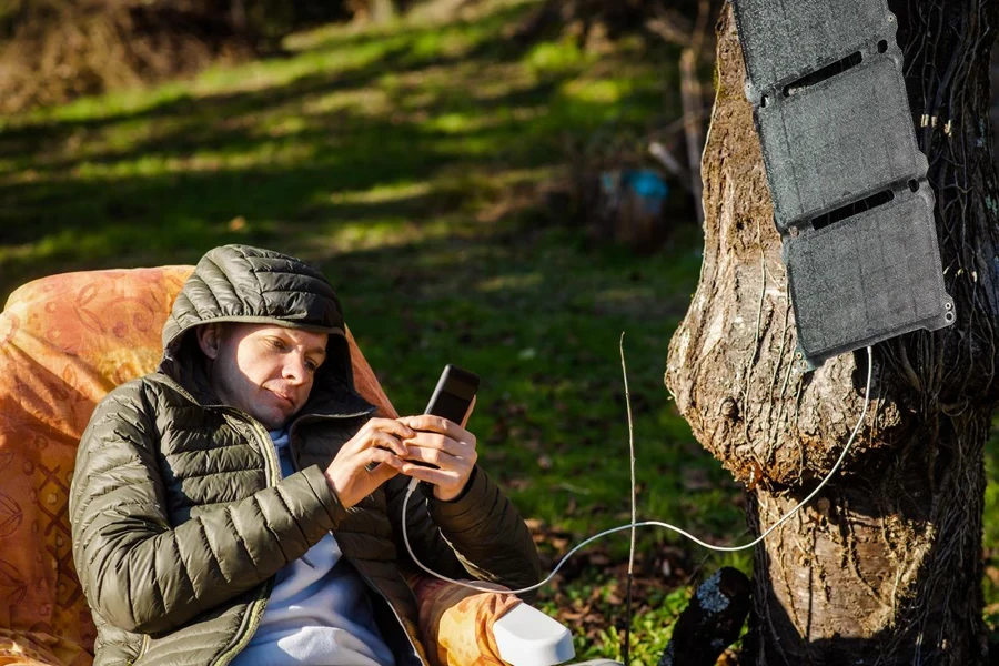 Campista carregando seu telefone usando uma bateria solar portátil