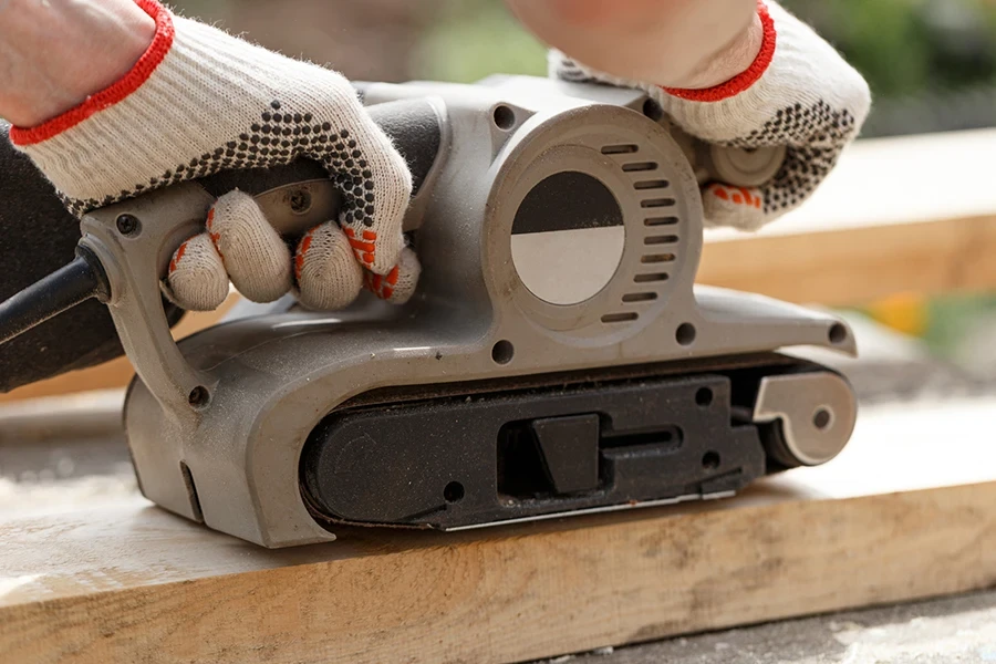 Carpenter sanding wood with belt sander in the garden