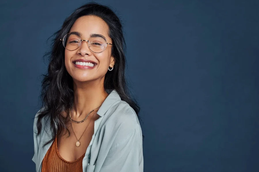 Casual young multiethnic woman with eyeglasses smiling at camera on blue background