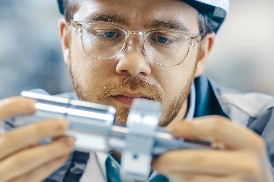 Primer plano del ingeniero industrial que usa clases y casco conecta dos componentes que diseñó. Precisión en ingeniería mecánica