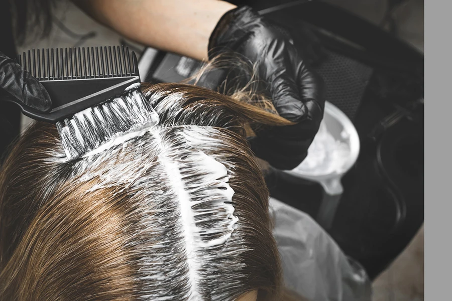 Close-up do colorista tinge o cabelo da mulher com escova e papel alumínio no salão de beleza