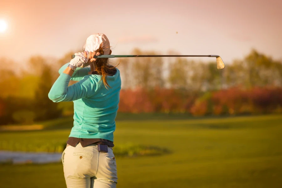 Gün batımında çim sahada golf sopasını sallayan kadın golf oyuncusunun yakın çekimi