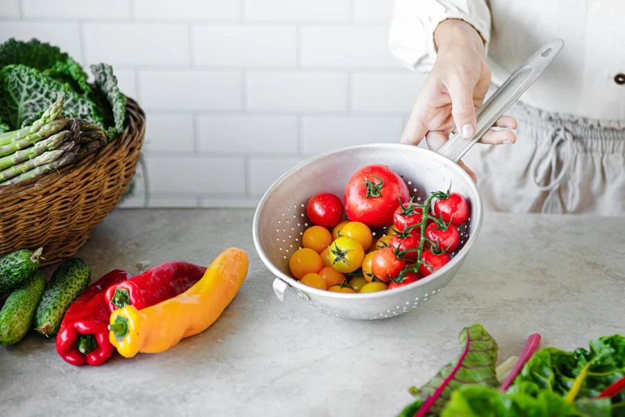 Close-up of woman hand holding colander with tomatoes over kitchen counter. 